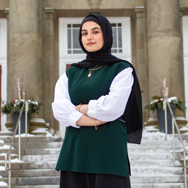 Mariam Knakriah stands on the steps of the entrance to the Henry Hicks Building with arms folded.