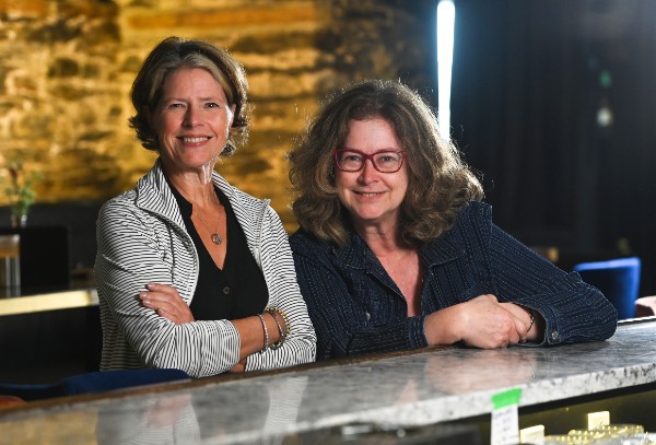 Lisa Murphy and Karen Spaulding leaning against a bar top in a restaurant, smiling.