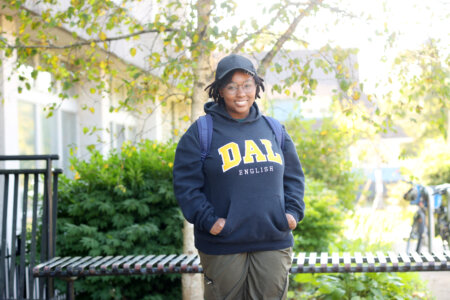 A university student wearing a black ballcap and DAL hoodie stands with hands in her pockets.